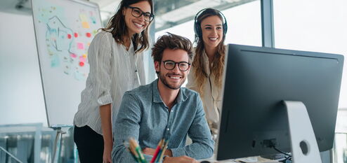 Drei junge Leute arbeiten gemeinsam lächelnd am Computer im modernen Büro
