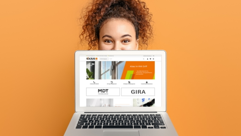 Frau hinter Laptop mit geöffneter Website auf orangefarbenem Hintergrund