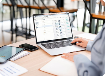 Person arbeitet am Laptop mit Perfion-Oberfläche am Schreibtisch, daneben Tablet, Smartphone und Notizblock