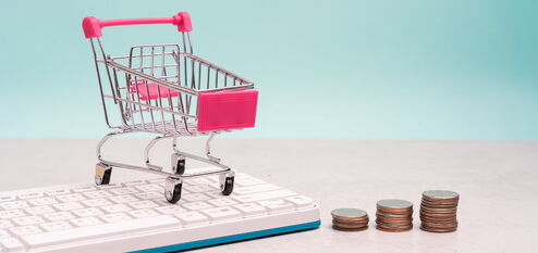 Mini-Einkaufswagen auf Tastatur neben gestapelten Münzen als Symbol für E-Commerce-Kosten