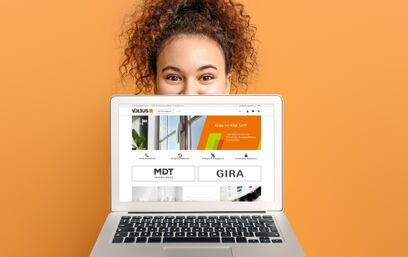 Frau hinter Laptop mit geöffneter Website auf orangefarbenem Hintergrund