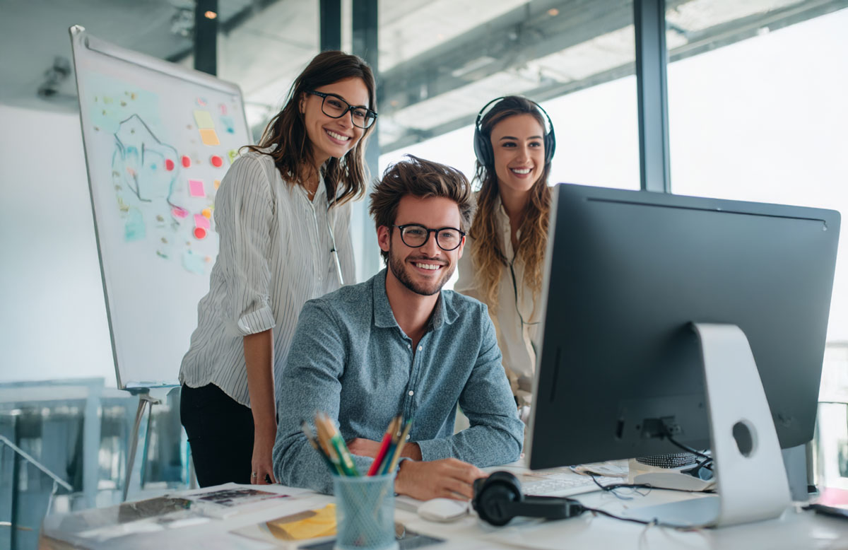 Drei junge Leute arbeiten gemeinsam lächelnd am Computer im modernen Büro